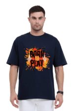 A man is wearing a navy blue unisex oversized T-shirt from Looga, featuring a dynamic graphic design with "Born to Play" in striking orange and white text, complemented by splatters and line details against a simple white backdrop.