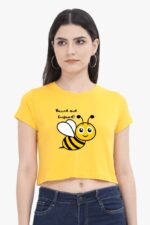 A woman confidently sports the "Buzzed and Confused" trendy woman crop top from Looga, featuring a vibrant yellow hue and a whimsical cartoon bee design. With her long dark hair cascading around hoop earrings, she effortlessly showcases a touch of style against a plain background.