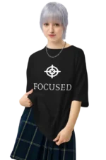 Person in black t-shirt with ‘FOCUSED’ print and plaid skirt pointing at shirt design.