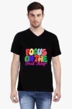 A man wearing a Looga Stylish V Neck T Shirt for Men, featuring vibrant text that reads "Focus on the Good Things," stands facing forward. He has short hair and is dressed in ripped blue jeans against a plain white background.