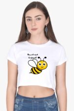 A woman with long brown hair wears the Trendy Woman Crop Top from Looga, which features a smiling cartoon bee and the text "Buzzed and Confused!" She completes her laid-back look with hoop earrings while standing against a plain background.