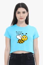 A person dressed in the Trendy Woman Crop Top by Looga, featuring a whimsical smiling bee illustration under the phrase "Buzzed and Confused," stands against a white background. They complete their playful, laid-back look with hoop earrings and black pants.