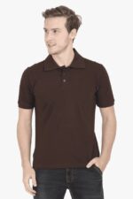 Dressed in a dark brown premium cotton polo shirt and dark jeans, a person strikes a casual pose against a plain backdrop. With short hair and one hand in their pocket, they look off to the side, exuding an air of thoughtful introspection akin to cool Looga fashion vibes.