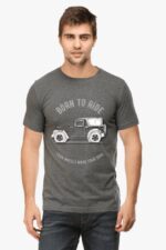 A man in a gray Thar Lovers T-Shirt with a vintage car design and Born to Ride, Four Wheels Move Your Soul text stands against a plain backdrop. His short hair complements the casual vibe of his blue jeans perfectly.