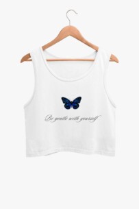 A white crop tank top with a blue butterfly graphic on the front, hanging on a wooden hanger against a plain background.