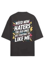 A back view of a black Premium Oversized T-Shirt featuring colorful Need new haters, the old ones are starting to like me text in Looga style, embellished with decorative stars and lightning bolts.