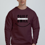 A person wearing a unisex oversized sweatshirt in a deep maroon color. The sweatshirt has a graphic print in the center.