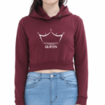 A person wearing a maroon crop hoodie with a crown graphic and the word QUEEN on the front, paired with light blue jeans, stands against a plain white background.