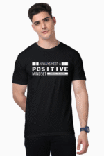 A man in a black Unisex Supima T-Shirt with Always Keep a Positive Mindset in white text stands before a plain white backdrop. Sporting short dark hair, he gazes directly at the camera with a neutral expression and an intriguing air of confidence.