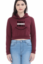 A woman with long dark hair wears a maroon Trendy Cropped Hoodie by Looga, featuring SMILE EVERYTIME and a smiley face graphic. She pairs it with light blue jeans and hoop earrings against a plain white background.