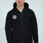 A person wears the Unisex Zip Hoodie - Comfort Meets Style, a black zip-up with a crest on the left, drawstrings, and front pockets, against a plain light-colored background showcasing its sleek looga style.