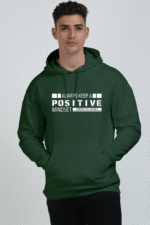 A person poses in a dark green Unisex Oversized Hooded Sweatshirt with a front pocket. The hoodie, set against a plain white background, features inspirational text in sleek Looga font: ALWAYS KEEP A POSITIVE MINDSET. EMBRACE THE JOURNEY.