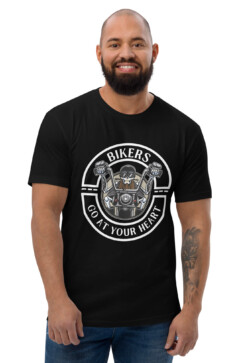 A bearded man smiles, wearing a Looga Black T-Shirt for Bikers - Comfort Meets Style, featuring motorcycle handlebars, a skull, and the phrase Bikers Go At Your Heart, showcasing his passion for the road. His tattooed right arm adds to his adventurous allure.