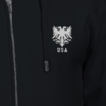 A person is seen from the chest up, wearing a black embroidered hoodie featuring a silver double-headed eagle emblem and USA text.