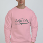 A person wearing a cozy oversized Light Baby Pink sweatshirt with Borcelle Legends Est. 1950 text, standing against a plain background.