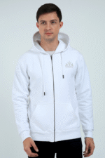 A person in the White1 hoodie, featuring a subtle logo on the upper left side, stands against a plain backdrop. The zip-up hoodie with pockets highlights its thick embroidered design. The individual with short dark hair gazes ahead.